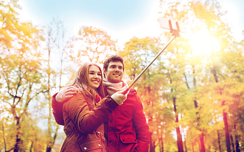 love, technology, relationship, family and people concept - happy smiling couple taking picture by smartphone selfie stick in autumn park