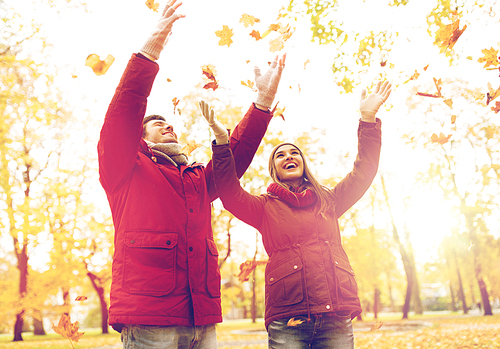 love, relationships, season and people concept - happy young couple throwing autumn leaves up in park