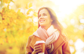 season, hot drinks and people concept - beautiful happy young woman drinking coffee or tea from disposable paper cup in autumn park