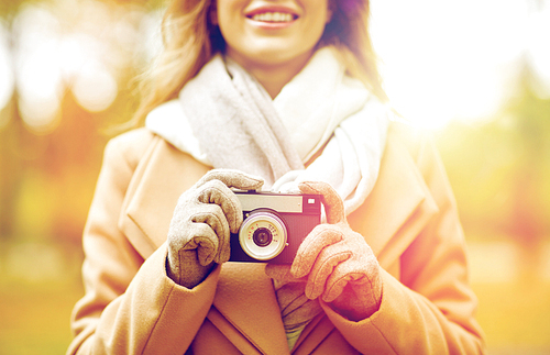 season, photography and people concept - close up of happy smiling young woman taking picture with vintage camera in autumn park