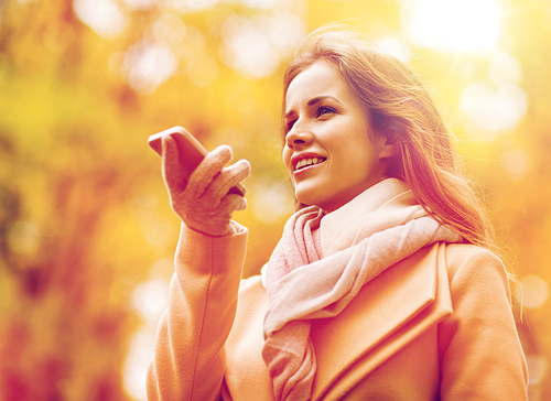 season, technology and people concept - beautiful young woman in autumn park and using voice command recorder on smartphone