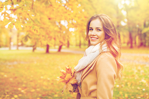 season and people concept - beautiful young woman with maple leaves walking in autumn park