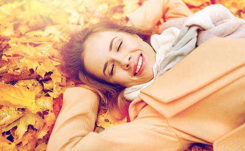 season and people concept - beautiful young woman lying on ground and autumn leaves