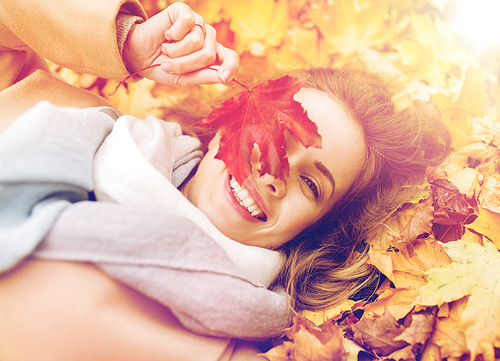 season and people concept - beautiful young woman with autumn maple leaf lying on ground