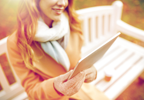 season, technology and people concept - close up of beautiful happy young woman with tablet pc computer sitting on bench in autumn park