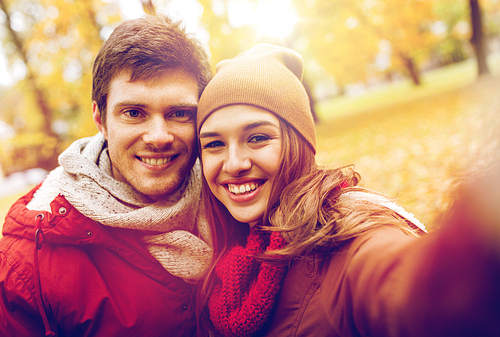 love, technology, relationship, family and people concept - happy smiling young couple taking selfie in autumn park