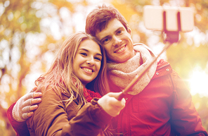 love, technology, relationship, family and people concept - happy smiling couple taking picture by smartphone selfie stick in autumn park