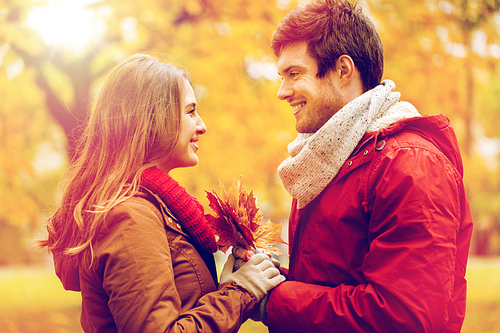 love, relationships, season and people concept - happy young couple with maple leaves in autumn park