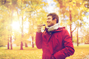 leisure, technology, communication and people concept - smiling hipster man using voice command recorder or calling on smartphone at autumn park