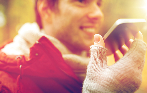 leisure, technology, communication and people concept - close up of smiling hipster man using voice command recorder or calling on smartphone in autumn