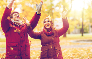 love, relationships, season and people concept - happy young couple throwing autumn leaves up in park