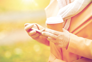 season, hot drinks and people concept - close up of woman with smartphone and disposable coffee or tea paper cup in autumn park