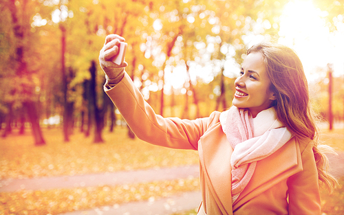 season, technology and people concept - beautiful young happy woman taking selfie with smartphone in autumn park