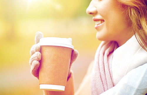 season, hot drinks, advertisement and people concept - close up of beautiful happy young woman drinking coffee or tea from disposable paper cup in autumn park