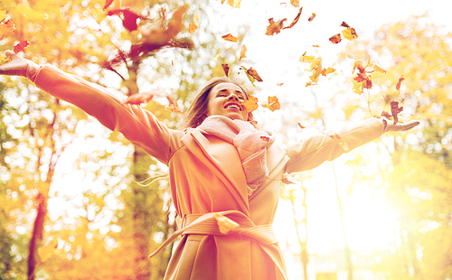 season and people concept - beautiful happy young woman having fun with leaves in autumn park