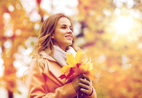 season and people concept - beautiful young woman with maple leaves walking in autumn park