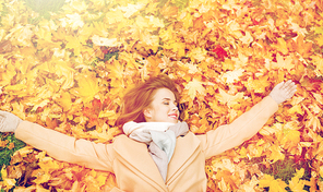 season and people concept - beautiful young woman lying on ground and autumn leaves