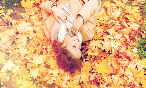 season and people concept - beautiful young woman lying on ground and autumn leaves