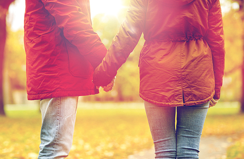 love, relationships, season and people concept - close up of happy young couple holding hands in autumn park