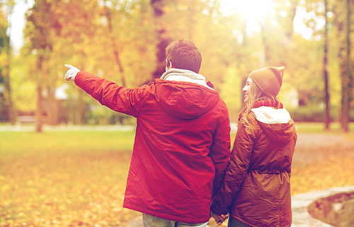 love, relationships, season and people concept - happy young couple walking in autumn park and pointing finger to something