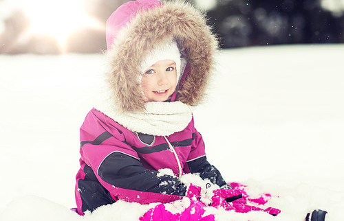 childhood, fashion, season and people concept - happy little kid in winter clothes playing with snow outdoors