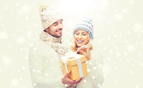 winter, holidays, couple, christmas and people concept - smiling man and woman in hats and scarf with gift box