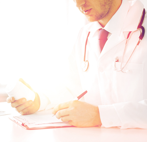 healthcare, hospital and medical concept - male doctor writing prescription paper and capsules