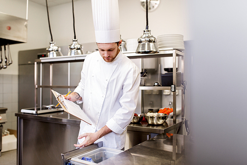 cooking, profession and people concept - male chef cook with clipboard doing inventory of restaurant kitchen fridge