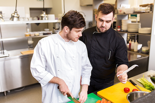 cooking food, profession and people concept - two happy male chefs looking to order or recipe at restaurant kitchen