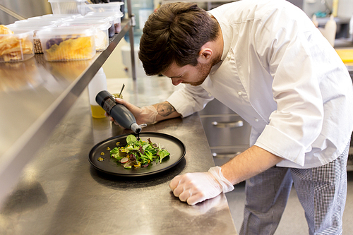 food cooking, profession and people concept - male chef cook serving plate of salad and seasoning it with balsamic vinegar sauce at restaurant kitchen