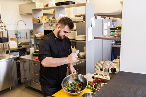 cooking food, profession and people concept - male chef cook making salad at restaurant kitchen