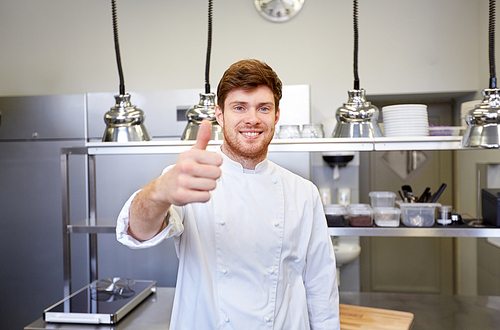 cooking, profession and people concept - happy male chef cook at restaurant kitchen showing thumbs up