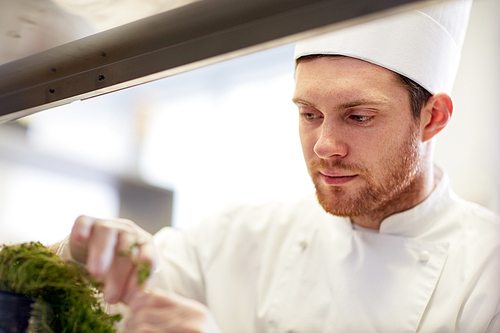 cooking, profession and people concept - happy male chef cook with greens making food at restaurant kitchen