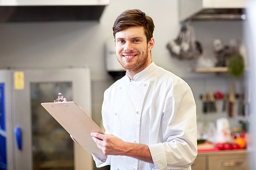 cooking, profession and people concept - happy smiling male chef cook writing to clipboard and doing inventory at restaurant kitchen