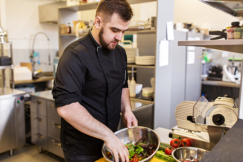 cooking food, profession and people concept - male chef cook making salad at restaurant kitchen