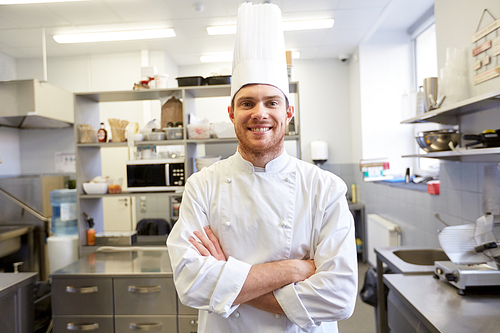 cooking, profession and people concept - happy male chef cook  in toque with crossed hands at restaurant kitchen