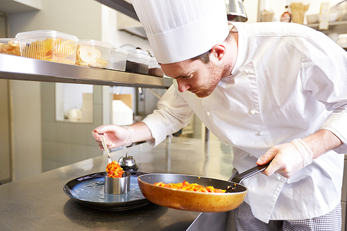food cooking, profession and people concept - happy male chef cook with frying pan and mold serving stewed vegetables on plate at restaurant kitchen