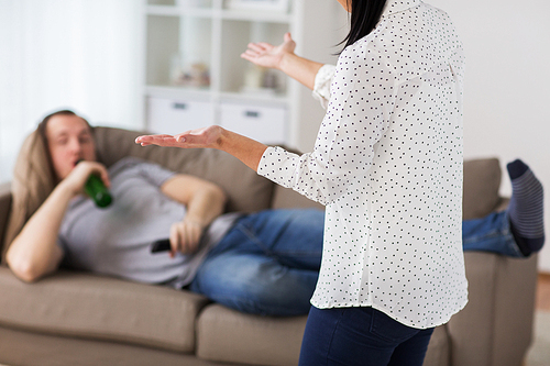 people, relationship difficulties, conflict and alcohol abuse concept - angry woman having argument with man drinking beer and watching tv at home