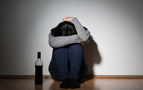alcoholism, depression and people concept - unhappy woman with bottle of alcohol crying at home