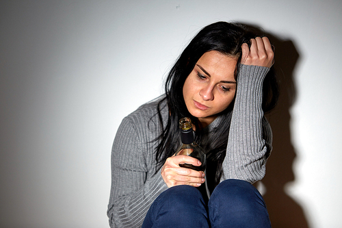 alcoholism, depression and people concept - unhappy drunk crying woman with bottle of alcohol