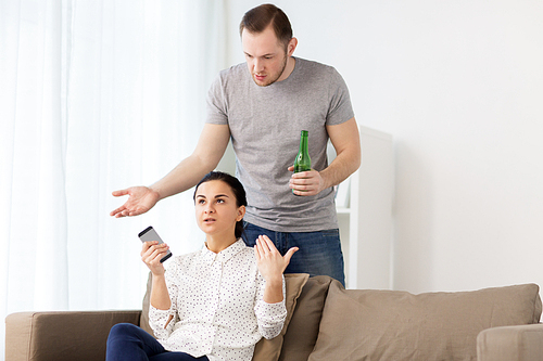 people, relationship difficulties and conflict concept - man drinking beer and woman with smartphone having argument at home