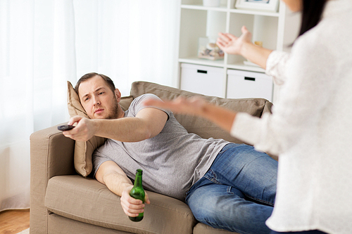 people, relationship difficulties, conflict and family concept - angry woman having agrument with man drinking beer and watching tv at home