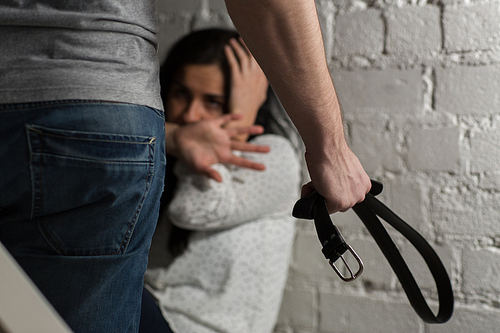 domestic violence, abuse and people concept - man beating helpless scared woman with belt