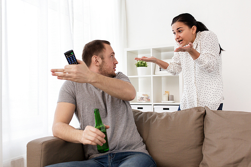 people, relationship difficulties, conflict and family concept - angry woman having argument with man drinking beer and watching tv at home