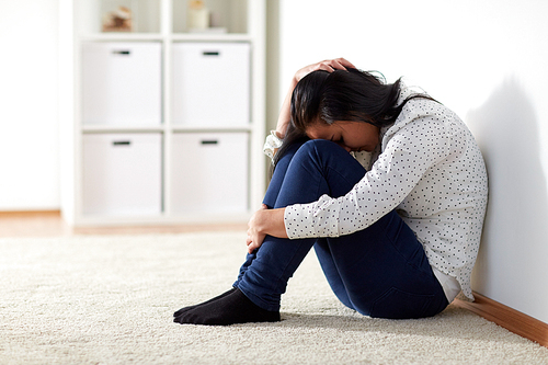 people, grief and domestic violence concept - unhappy woman sitting on floor and crying at home