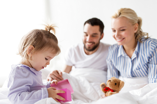people, family, holidays and morning concept - happy little girl and parents with gift box in bed at home