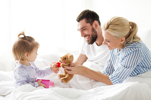 people, family, holidays and morning concept - happy little girl and parents with gift box in bed at home