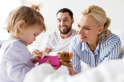 people, family, holidays and morning concept - happy little girl and parents with gift box in bed at home