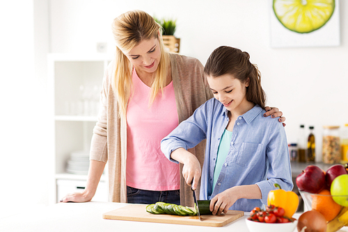 cooking food, healthy eating, family and people concept - happy mother and daughter chopping vegetables for dinner at home kitchen