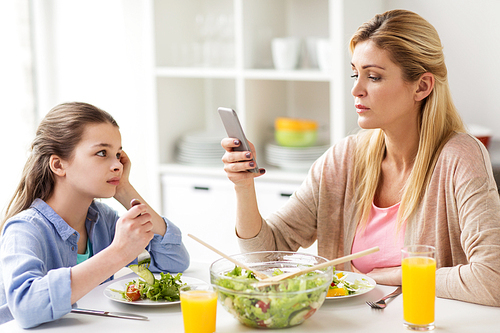 family, communication and people concept - sad girl looking at her mother with smartphone having dinner at home
